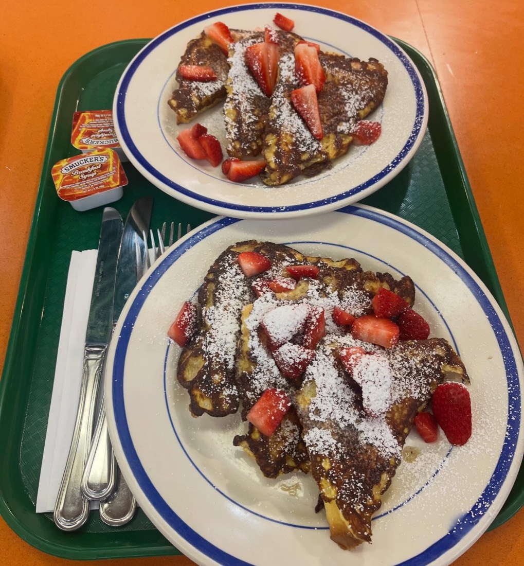 Two plates of French toast topped with fresh strawberries and powdered sugar on a green tray.
